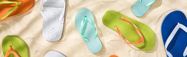 Panoramic shot of scattered white, turquoise, green and blue flip flops on sand — Stock Photo