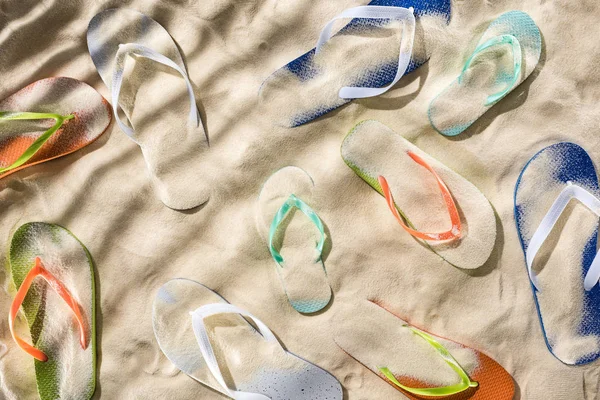 Draufsicht auf verstreute türkisfarbene, orangefarbene, blaue und grüne Flip Flops auf Sand mit Schatten — Stockfoto