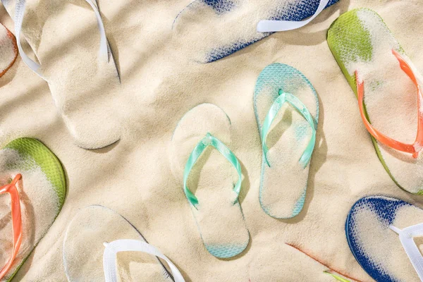 Top view of scattered turquoise, orange, blue and green flip flops on sand — Stock Photo