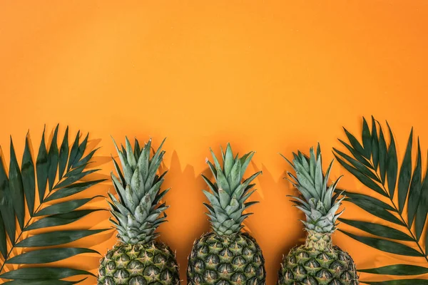 Top view of pineapples and tropical leaves on orange background with copy space — Stock Photo