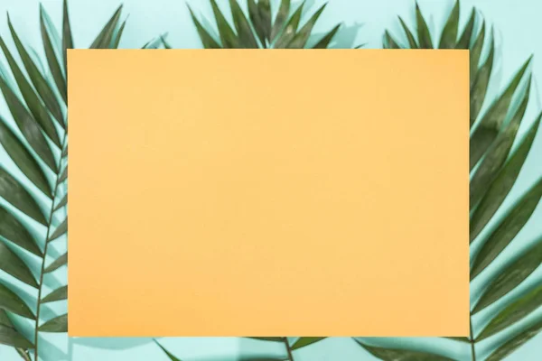 Top view of tropical leaves and empty orange card on turquoise background — Stock Photo