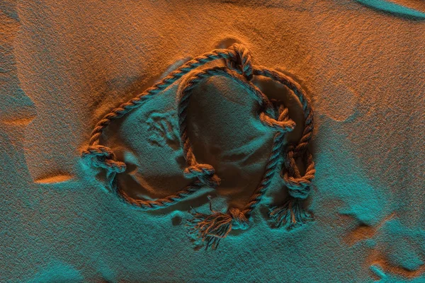 Vue de dessus de la corde courbée avec des nœuds sur le sable avec des lumières orange et bleu — Photo de stock