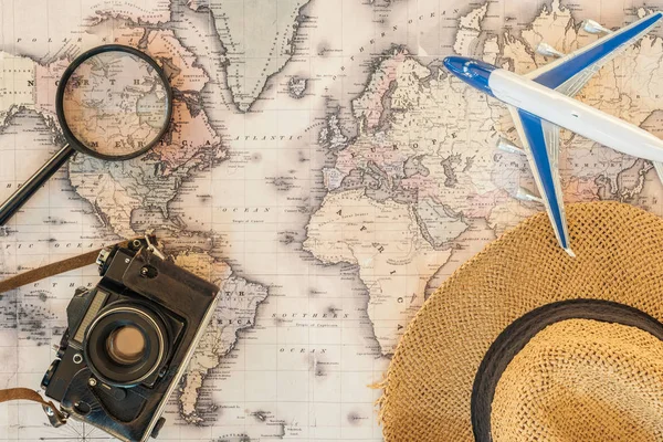 Vista superior del sombrero de paja, lupa, avión de juguete y cámara de película en el mapa del mundo - foto de stock