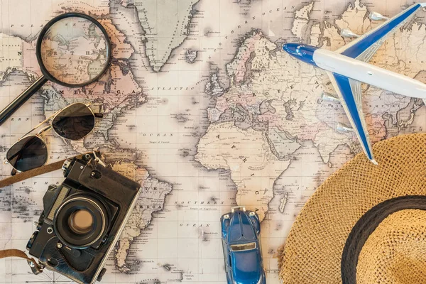 Vista superior del sombrero de paja, lupa, gafas de sol, coche de juguete, avión de juguete y cámara de película en el mapa del mundo - foto de stock