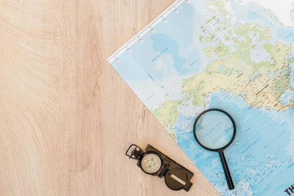 Vue du dessus de la carte du monde, loupe et compas sur la surface en bois — Photo de stock