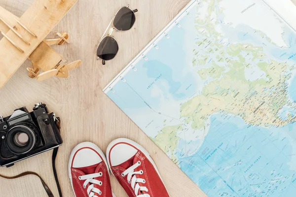 Vista superior de zapatos de goma rojos, cámara de cine, avión de juguete, gafas de sol y mapa del mundo en superficie de madera - foto de stock
