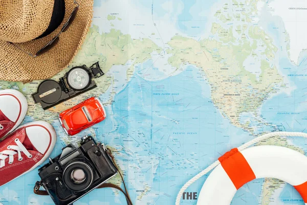 Vista superior de gumshoes, câmera de filme, chapéu de palha, óculos de sol, carro de brinquedo, bússola e bóia de salvação no mapa do mundo — Fotografia de Stock