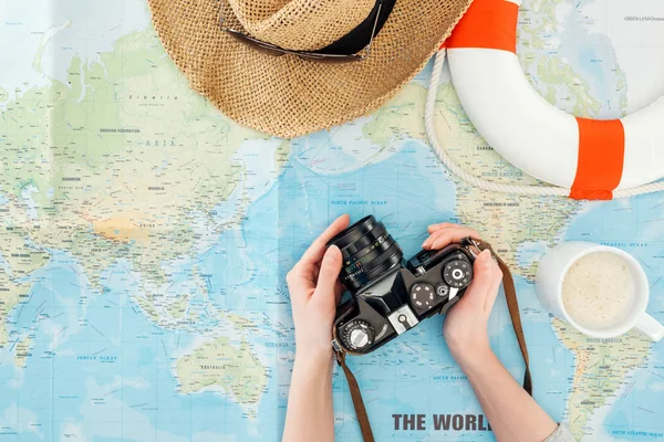 Vue recadrée de la femme avec chapeau de paille et bouée de sauvetage tenant la caméra de film sur la carte du monde — Photo de stock