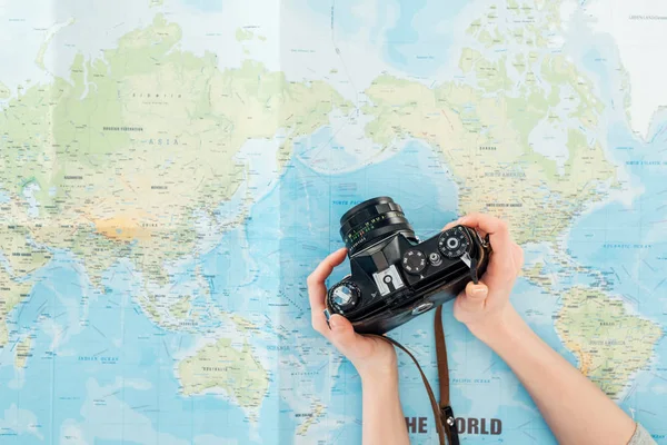 Vista recortada de la mujer sosteniendo la cámara de película en el mapa del mundo - foto de stock