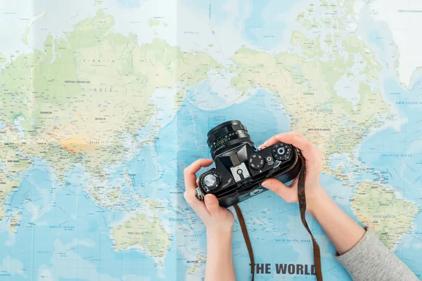 Vista recortada de la mujer sosteniendo la cámara de película en el mapa del mundo - foto de stock