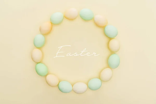 Top view of round frame made of painted chicken eggs on light yellow background with Easter lettering — Stock Photo