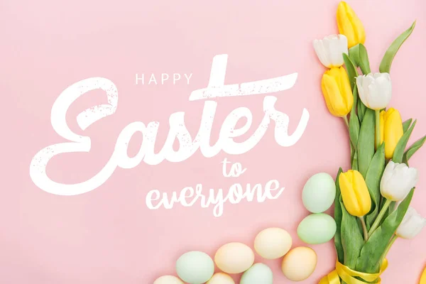 Ansicht von bemalten Hühnereiern und hellen Tulpen auf rosa Hintergrund mit frohen Ostern für alle Schriftzug — Stockfoto