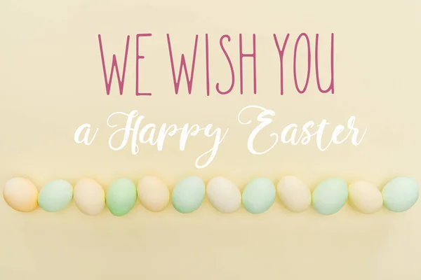 Top view of painted pastel chicken eggs on light yellow background with we wish you a happy Easter lettering — Stock Photo