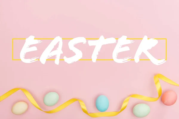 Top view of painted multicolored chicken eggs and satin ribbon on pink background with Easter lettering — Stock Photo