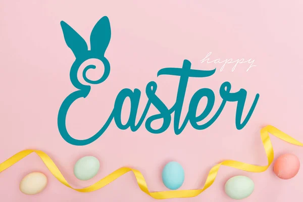 Top view of painted multicolored chicken eggs and satin ribbon on pink background with happy Easter blue lettering — Stock Photo