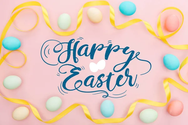 Top view of painted multicolored chicken eggs and satin yellow ribbon on pink background with happy Easter lettering — Stock Photo