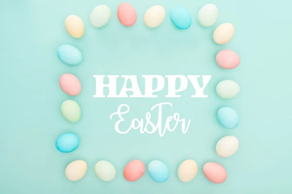 Top view of square frame made of painted chicken eggs on blue background with happy Easter lettering — Stock Photo