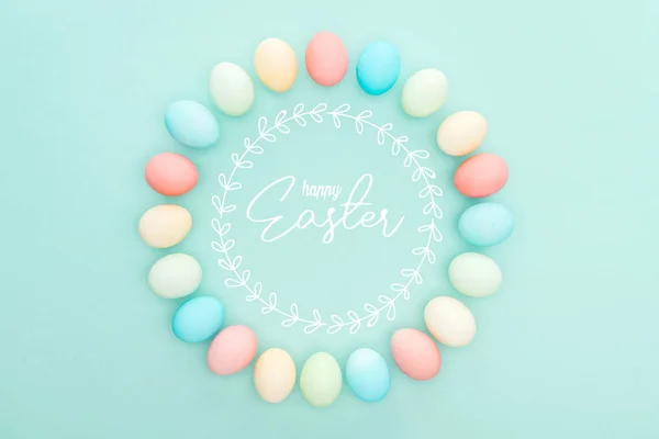 Top view of round frame made of painted chicken eggs on blue background with happy Easter lettering — Stock Photo