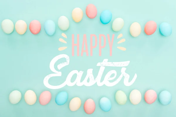 Top view of painted chicken eggs on blue background with happy Easter lettering — Stock Photo