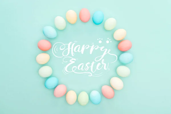 Top view of round frame made of painted chicken eggs on blue background with white happy Easter lettering — Stock Photo