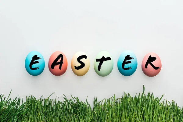 Top view of painted chicken eggs with Easter word near green grass on grey background — Stock Photo