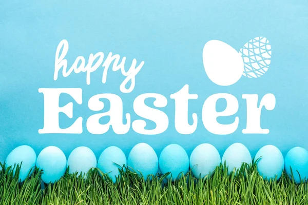 Blue painted chicken eggs on green grass with happy Easter white lettering on blue background — Stock Photo