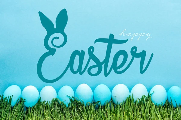 Blue painted chicken eggs on green grass with happy Easter lettering on blue background — Stock Photo