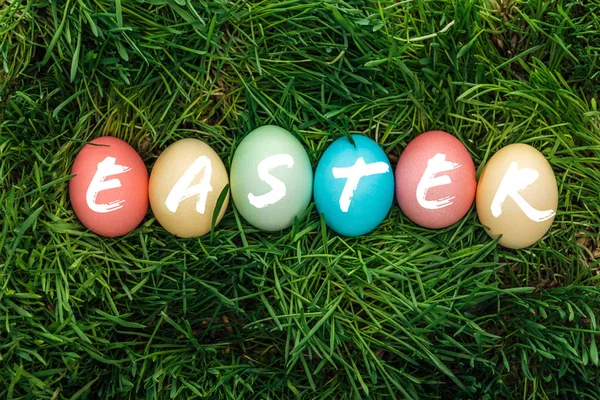 Top view of painted multicolored eggs with Easter word on green grass — Stock Photo