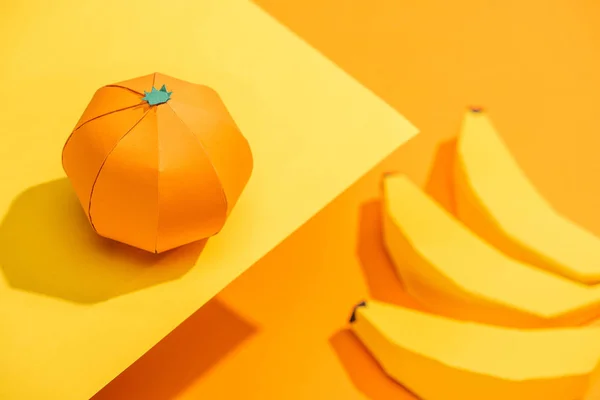Enfoque selectivo de la mandarina de origami sobre papel amarillo con plátanos de cartón sobre naranja - foto de stock