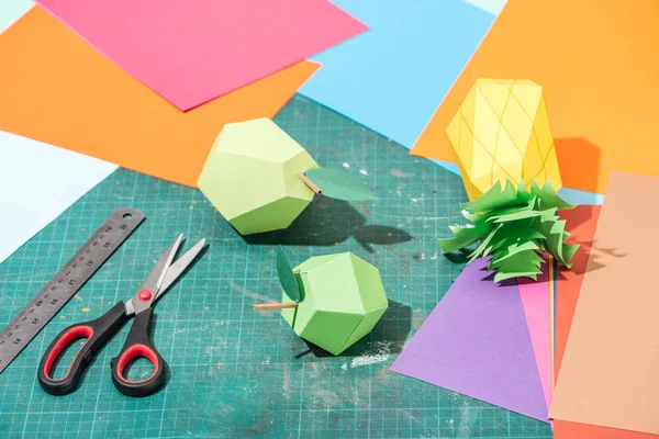 Origami fruits and colorful cardboard with scissors and ruler on messy surface — Stock Photo