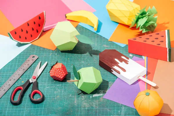 Origami fruits and colorful cardboard with scissors and ruler on messy surface — Stock Photo