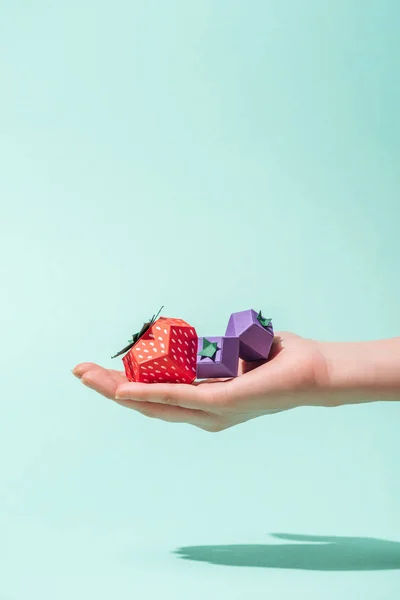 Cropped view of young woman holding paper strawberry and blueberries on turquoise with copy space — Stock Photo