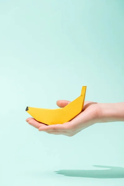 Cropped view of young woman holding paper banana on turquoise with copy space — Stock Photo
