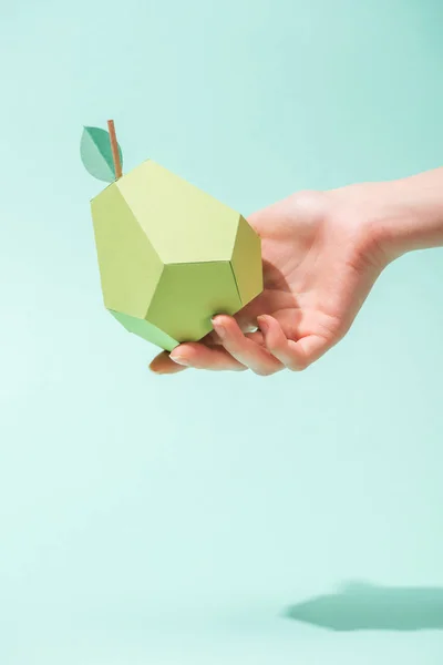 Cropped view of young woman holding handmade paper pear on turquoise — Stock Photo