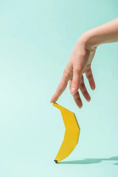 Cropped view of young woman touching paper banana on turquoise with copy space — Stock Photo