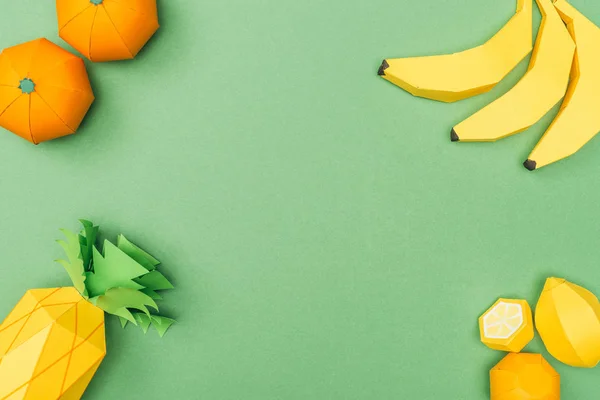 Vista superior de plátanos de papel hechos a mano, limones, mandarinas y piña aislados en verde - foto de stock
