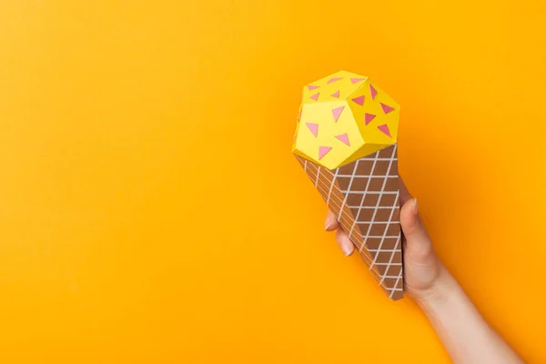 Vista cortada de jovem segurando cone de sorvete de papel isolado em laranja com espaço de cópia — Fotografia de Stock