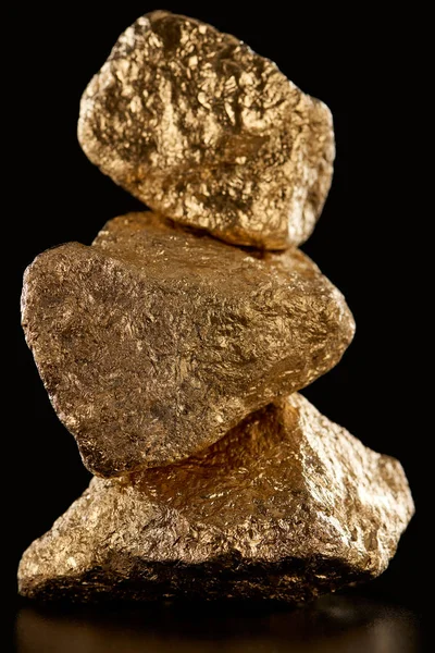 Vista de cerca de tres piedras brillantes texturizadas de oro aisladas en negro - foto de stock