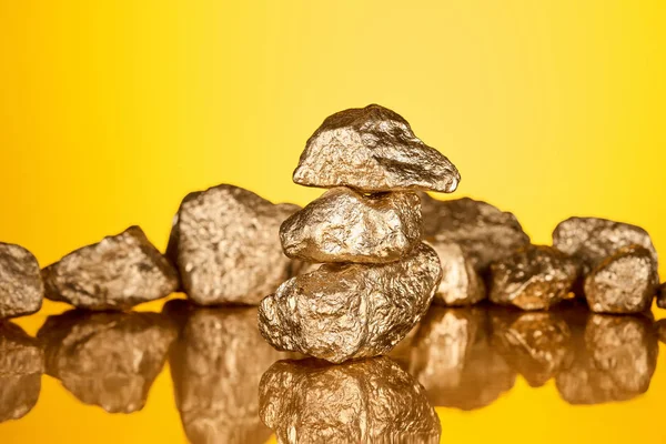 Селективное фокусирование трех блестящих золотых камней с отражением, изолированным на желтом — стоковое фото