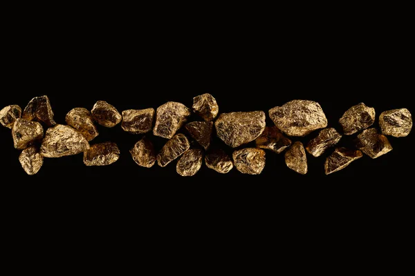 Vue de dessus de pierres texturées dorées disposées en rangée isolées sur noir — Photo de stock