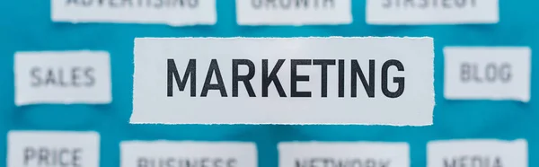 Panoramic shot of marketing word on pieces of paper on blue — Stock Photo