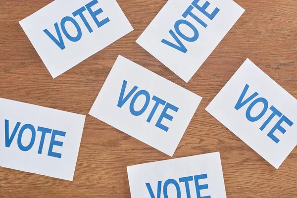 Vue du dessus des cartes blanches avec lettrage de vote bleu éparpillé sur la table en bois — Photo de stock