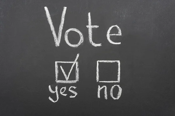 Top view of white vote lettering and check mark near yes word on black chalkboard — стоковое фото