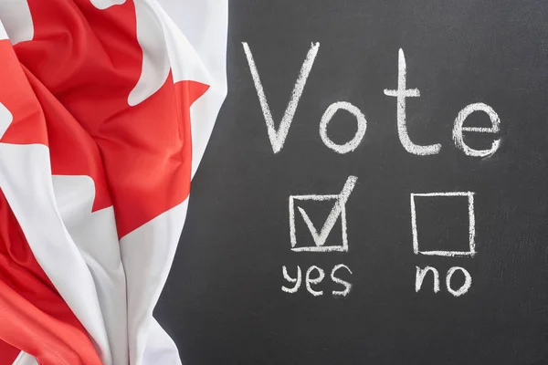 Ansicht von oben weißer Wahlschriftzug und Häkchen bei Ja Wort auf schwarzer Tafel in der Nähe der kanadischen Flagge — Stockfoto