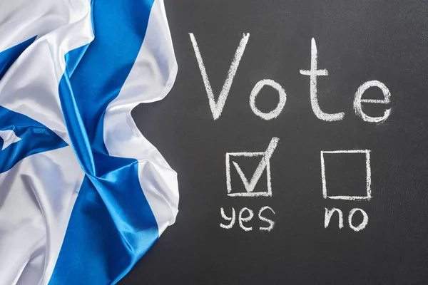 Top view of vote lettering and check mark near yes word on black chalkboard near crumpled flag of Israel — стоковое фото
