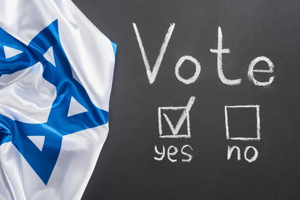 Ansicht von oben weißer Wahlschriftzug und Häkchen bei Ja Wort auf schwarzer Tafel in der Nähe der israel Flagge — Stockfoto