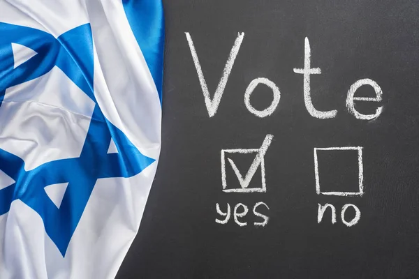 Top view of vote lettering and check mark in square near yes word on black chalkboard near flag of Israel — Stock Photo