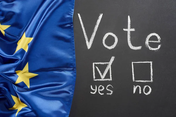 Top view of vote lettering and check mark near yes word on black chalkboard near flag of Europe — Stock Photo