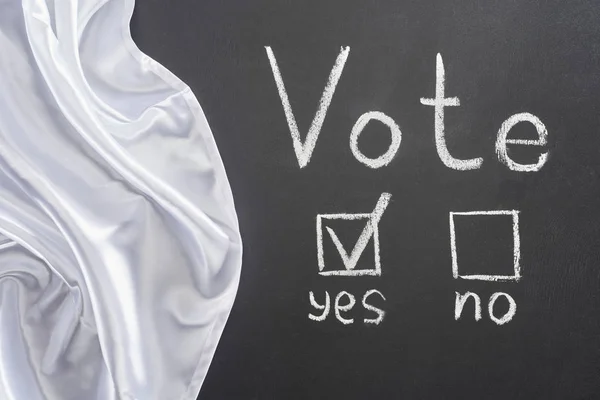 Top view of vote lettering and check mark near yes word on black chalkboard near white flag — Stock Photo