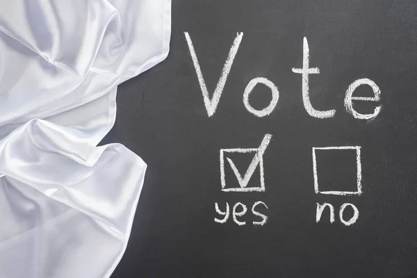 Top view of white vote lettering and check mark near yes word on black chalkboard near white flag — Stock Photo